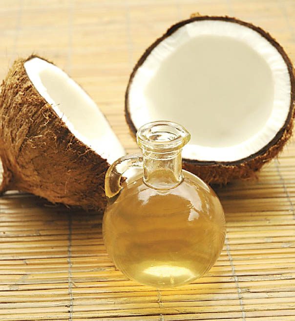 A bottle of wood-pressed coconut oil beside fresh coconut halves